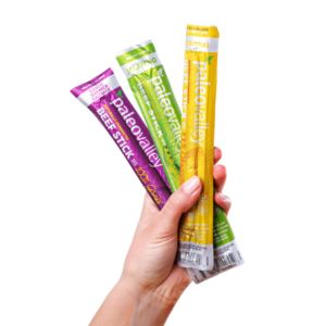 Hand holding three Paleo Valley meat sticks in beef and chicken flavors.