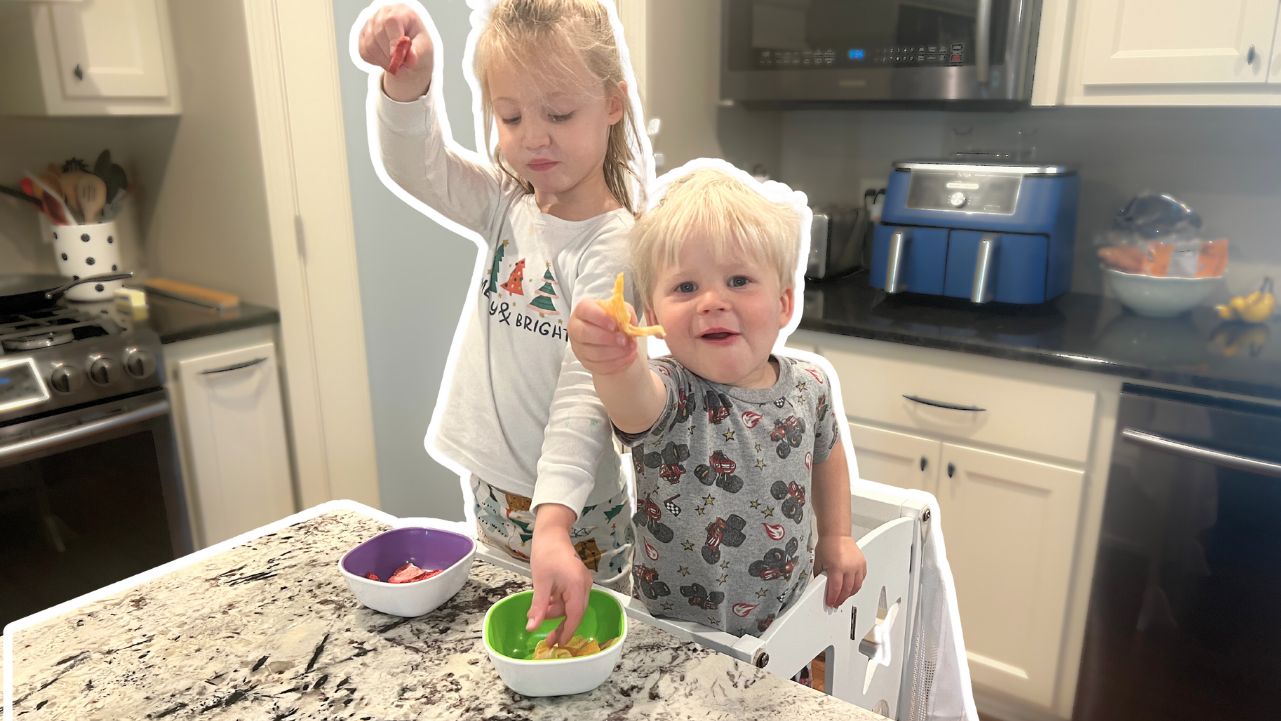 Two kids in the kitchen holding freeze-dried fruit.