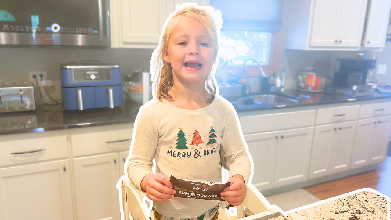 A little girl in a kitchen holding a Paleovalley protein bar.