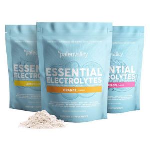 Three light blue bags of Paleovalley Essential Electrolytes with a small pile of electrolyte powder in the foreground.