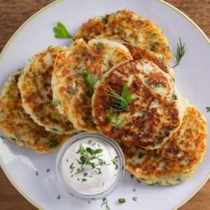 Loaded mashed potato pancakes with sour cream and garnish on a white plate.