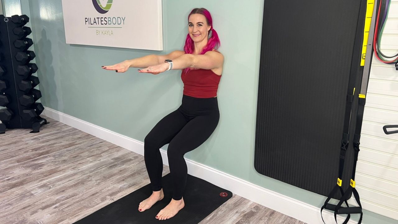 Pilatesbody by Kayla demonstrating the beginner Wall Pilates wall sit exercise.