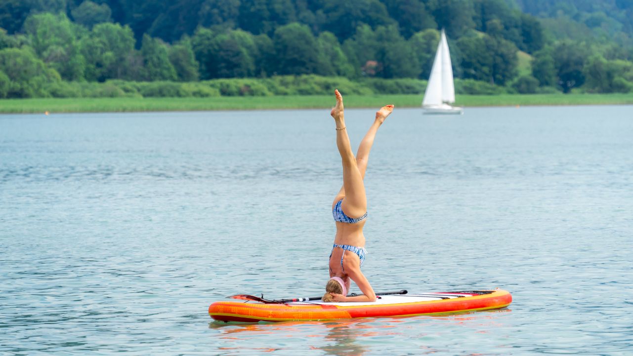 A woman doing a handstand on a paddleboard on a lake.