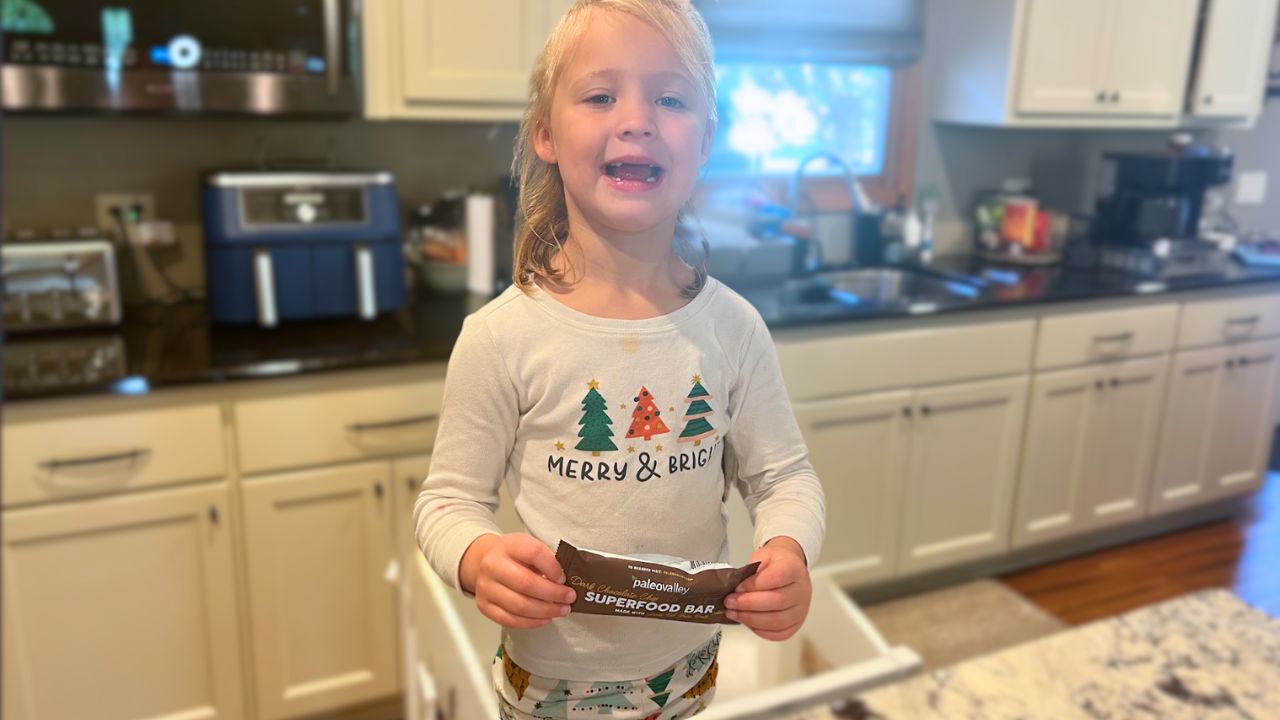 Little girl holding a Paleovalley Superfoods bar in the kitchen.