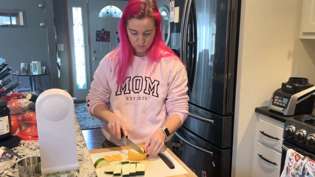Pilatesbody by Kayla chopping vegetables in the kitchen.