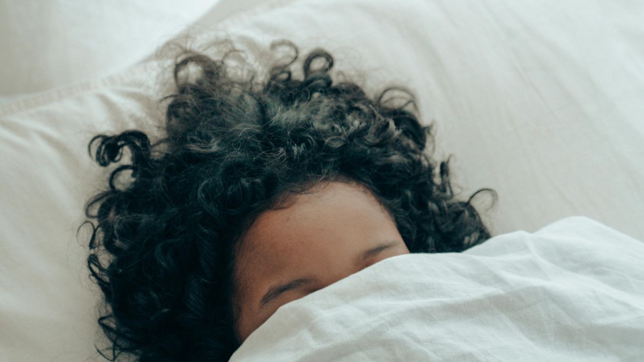 Bedtime ritual for better sleep A woman sleeping with a white sheet pulled up over her eyes.