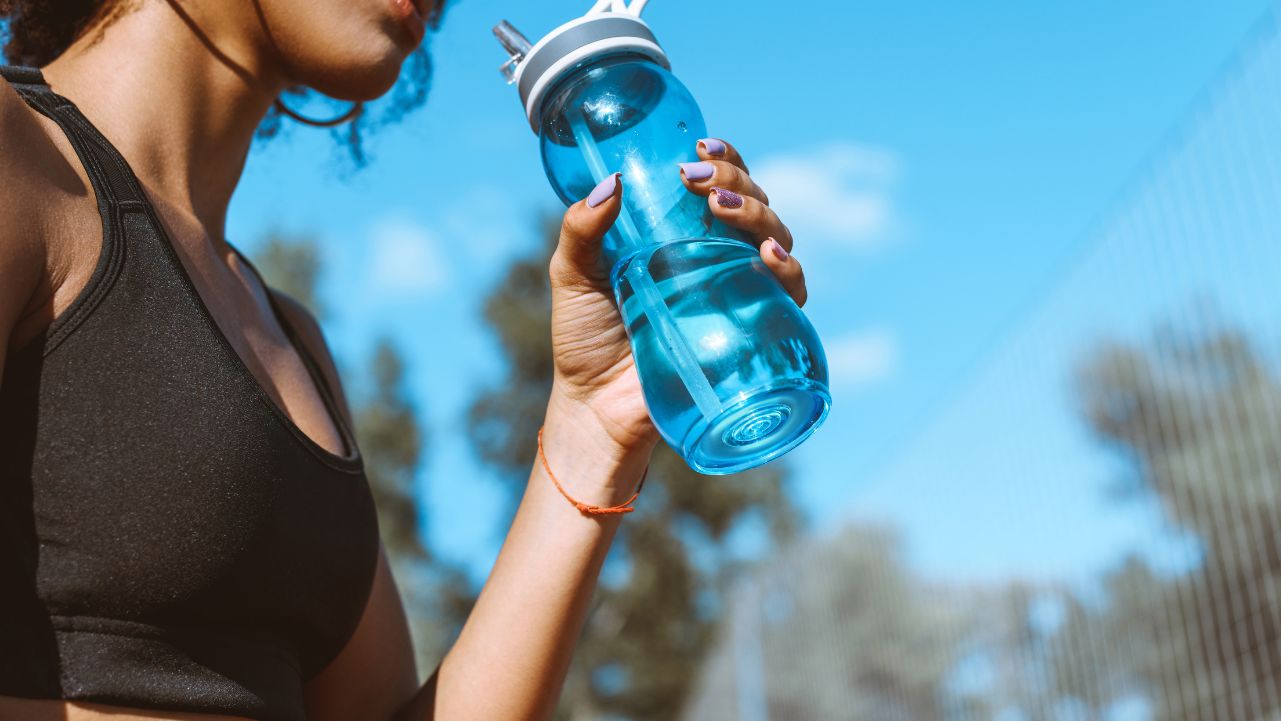 Wellness Routine A woman in a black sports bra drinking from a water bottle.