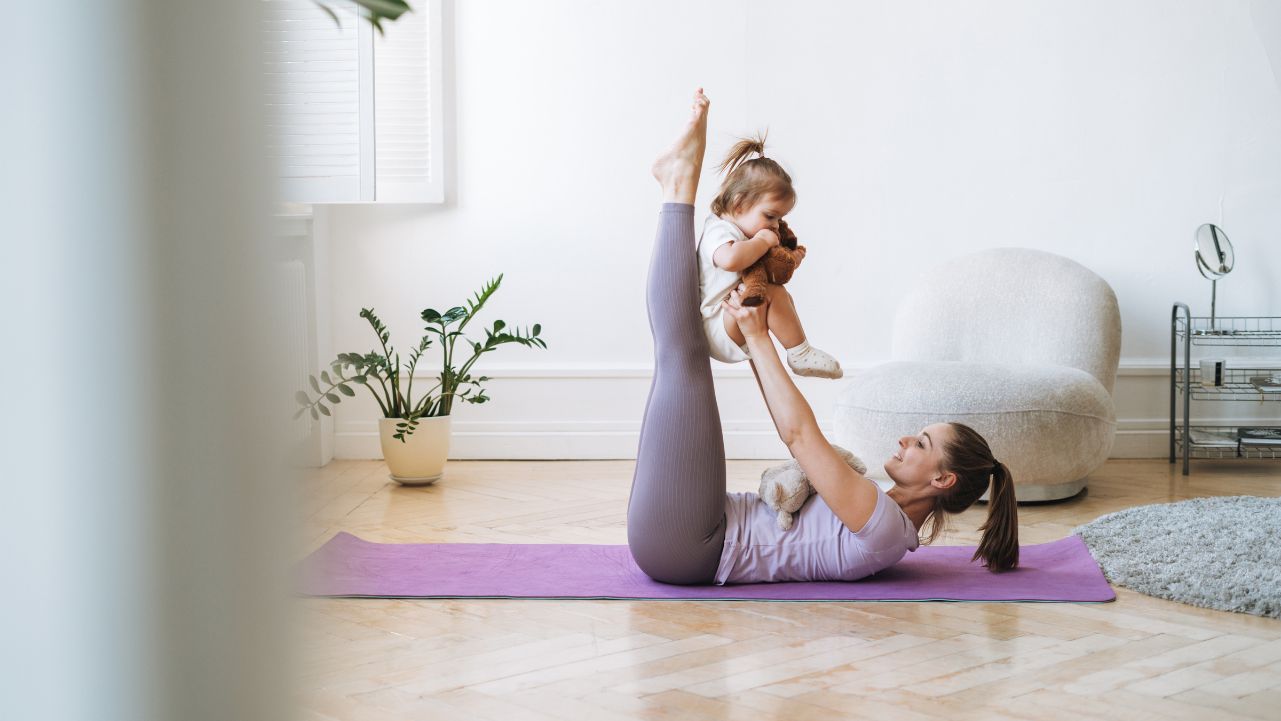 Staying active during busy times A mom lying on a yoga mat with her legs in the air holding a baby in her outstretched arms.