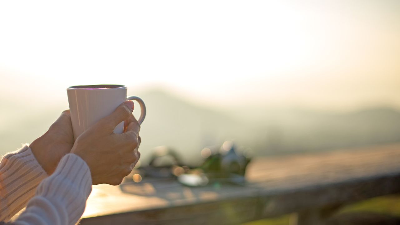 Hands holding a warm cup of coffee outdoors during a mindful morning routine.