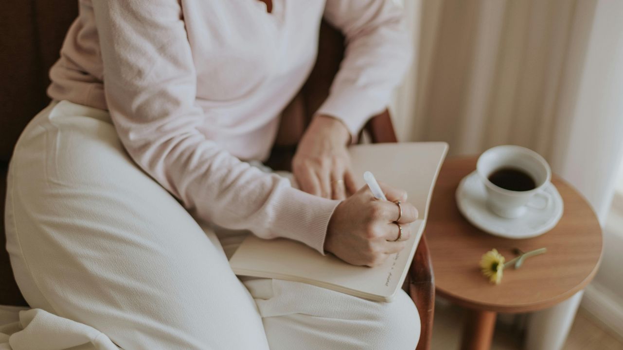 Woman writing in a journal with coffee nearby, learning how to change your habits with intention.