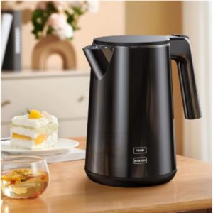 A black electric kettle on a counter top next to a slice of cake and a cup of tea.