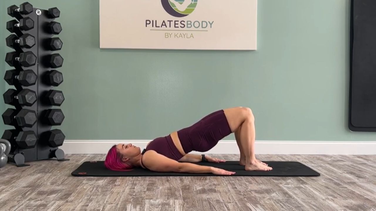 Pilatesbody by Kayla demonstrates how the Pilates shoulder bridge exercise is easy to do outside.