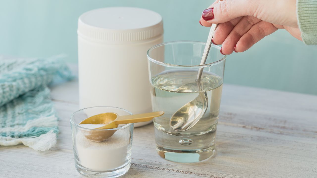 A woman's hand stirring collagen and colostrum supplements into a glass of water.