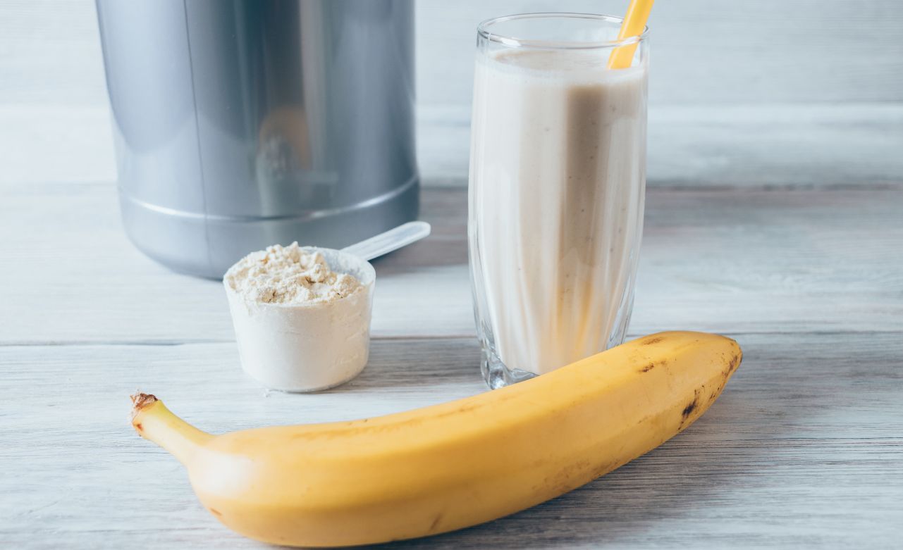 A banana, a scoop of protein powder, and a protein shake in a glass