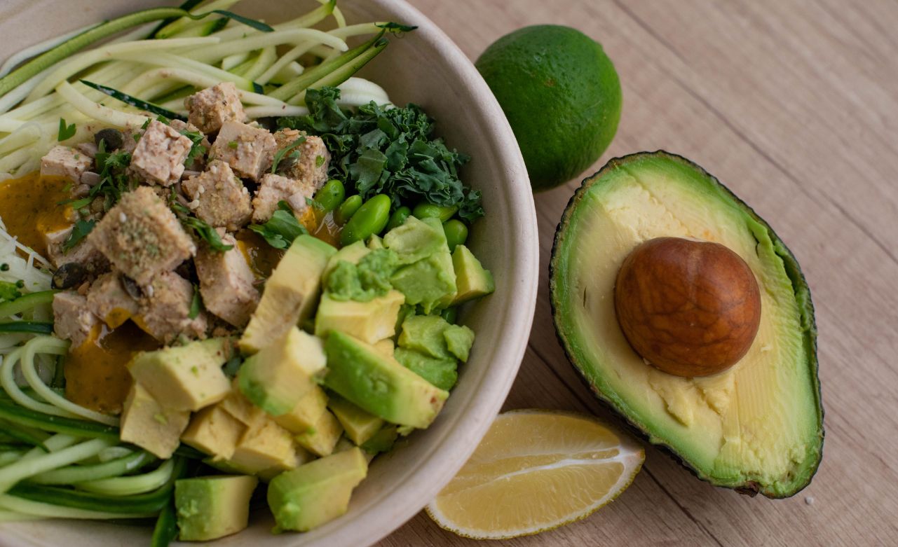 A bowl of salad with chicken and avocado chunks next to half an avocado and a lime